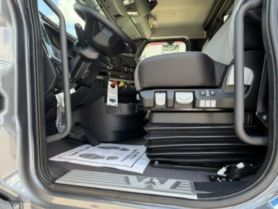 Cab view of a new 2027 Western Star 47X with steering wheel, dashboard, and operator seat; documents on floor mat; steps and entry sill visible.