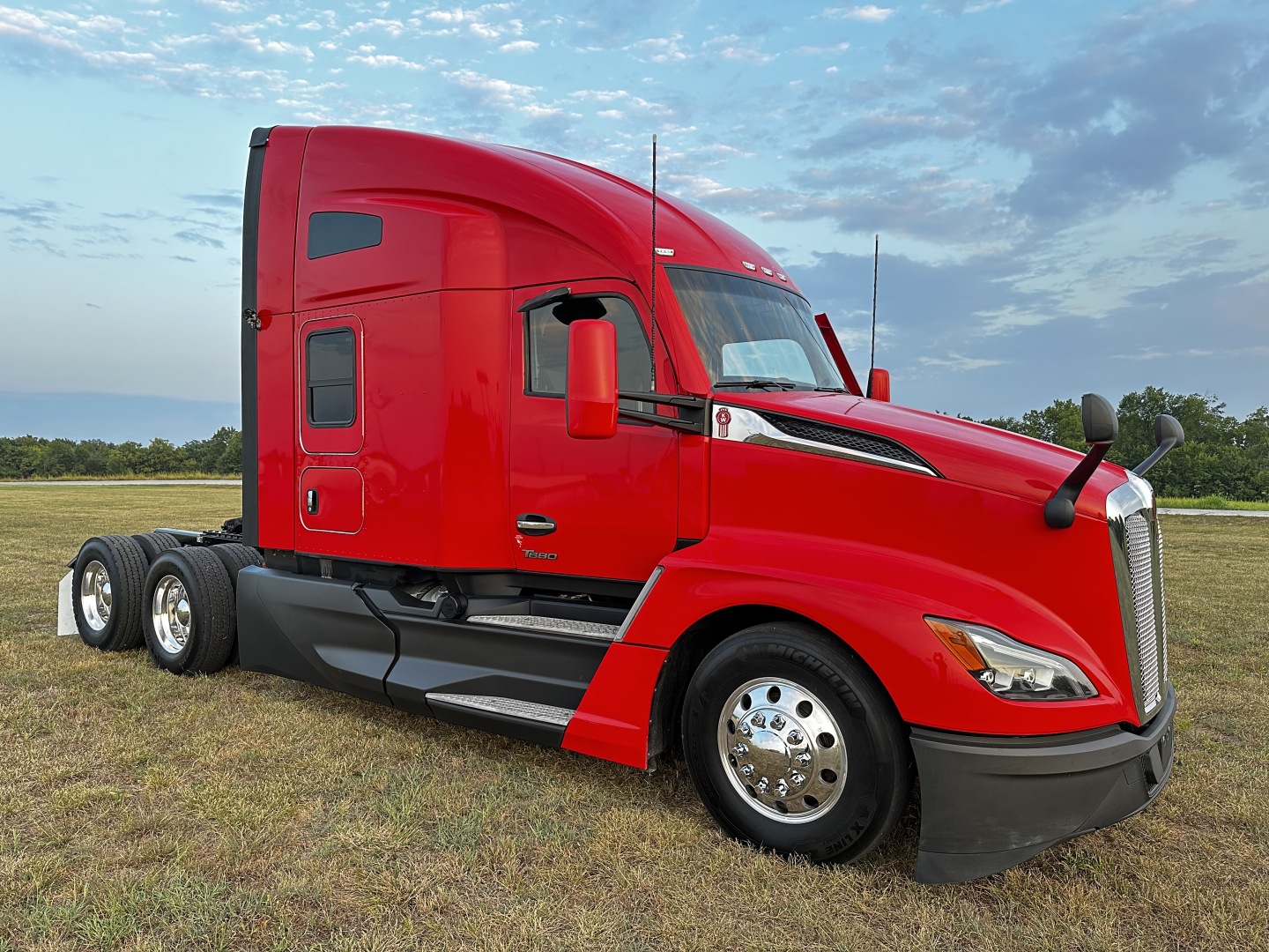 Red Kenworth T680 tractor-trailer cab, side view, with dual rear axles and chrome wheels.