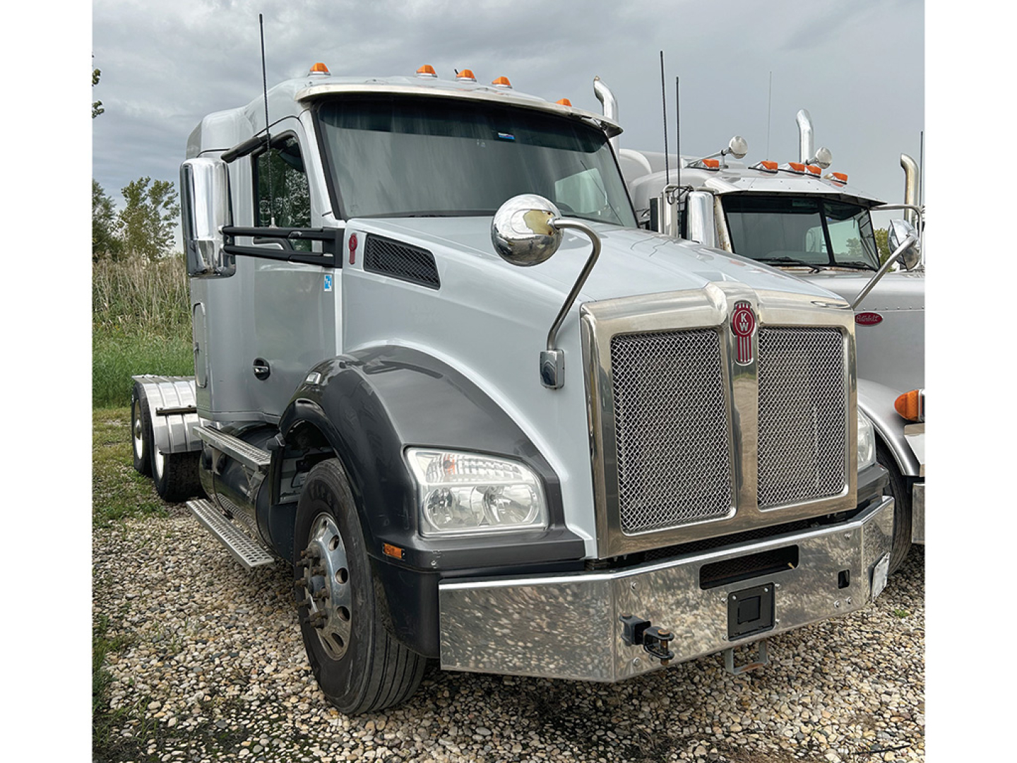 Kenworth T-880 conventional daycab truck in silver with large chrome grille and bumper, front view.