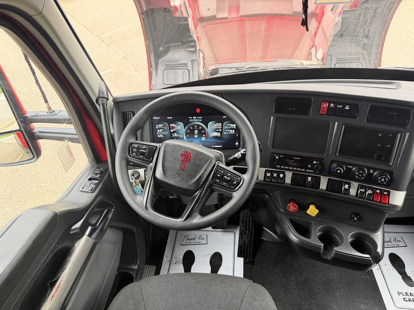 Kenworth T680 cab interior showing steering wheel with logo, dashboard with multiple gauges, center console with screens, and gear pedals.