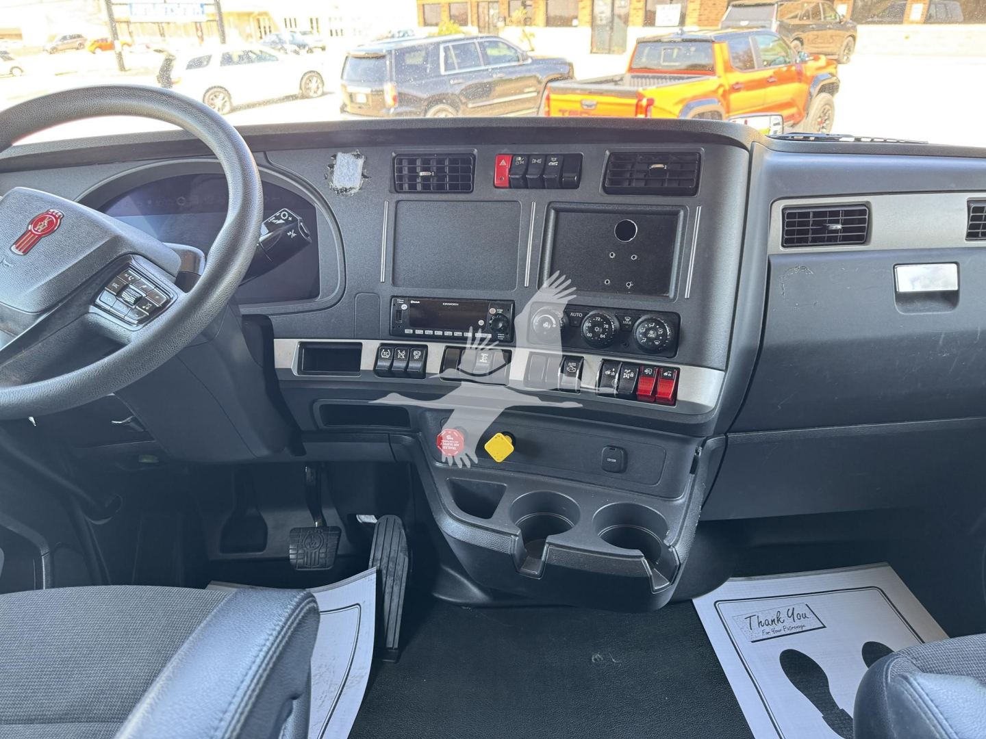 Kenworth T680 dashboard and steering wheel view showing instrument cluster, center console, and cup holders.