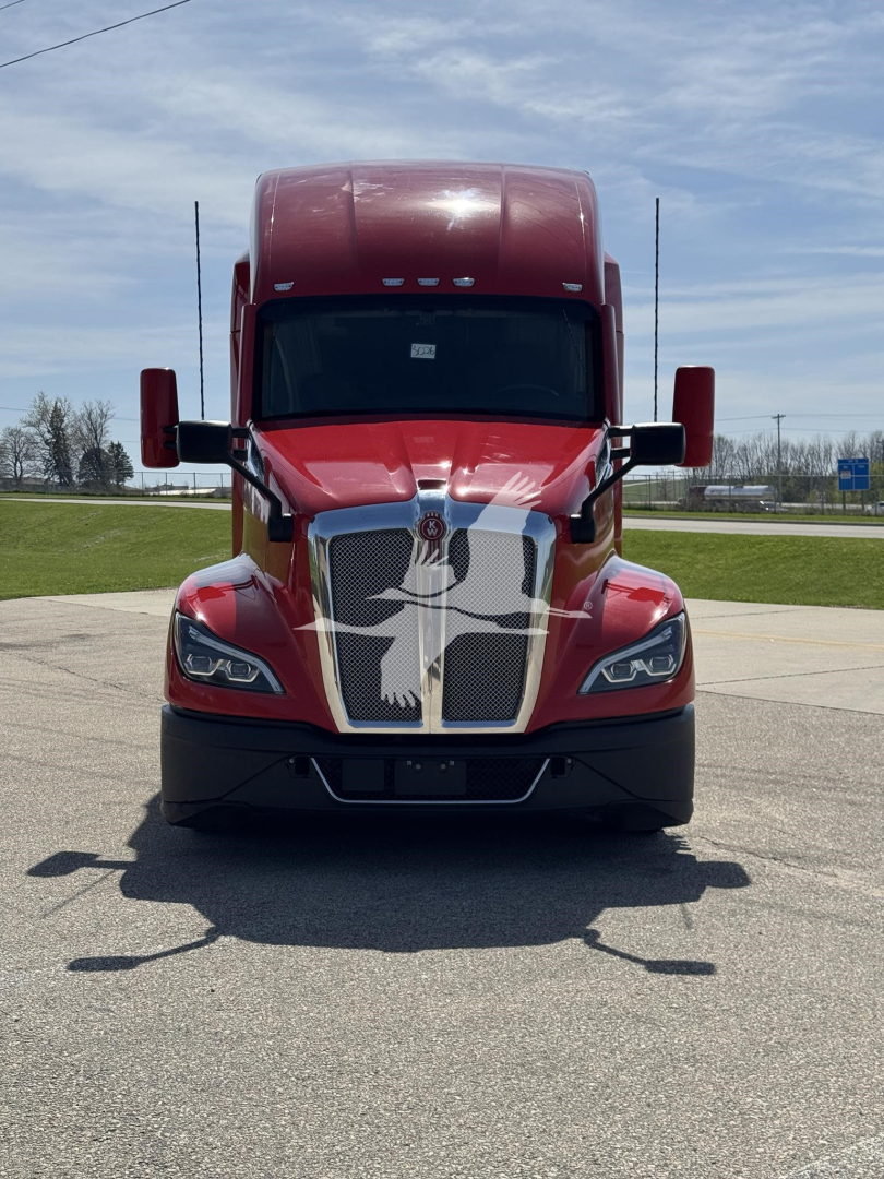 Kenworth T680 front view showing bold chrome grille, red cab with large hood, black bumper, side mirrors, and headlights.