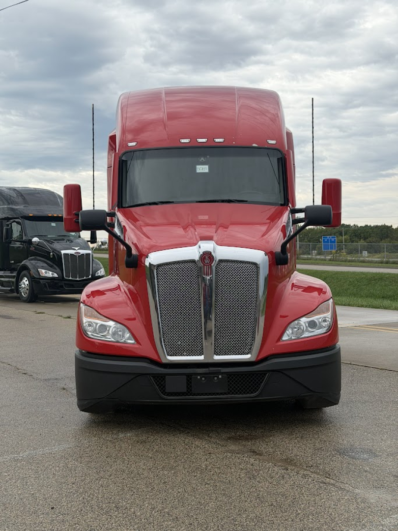 Kenworth T680 front view showing large chrome grille, red cab, black bumper, and dual side mirrors.