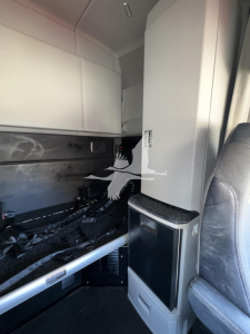 Cab interior of a Kenworth T680 sleeper truck showing an upper bunk area and a vertical storage cabinet with a small sink/console; limited legible text not visible.