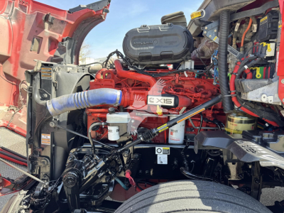 Kenworth T680 engine bay with a red engine and Cummins ISX15 label visible; air intake hose; coolant reservoir; filters; various hoses and wiring.