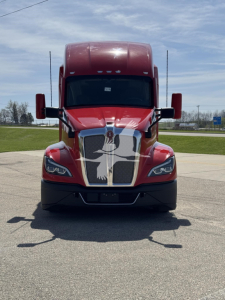 Kenworth T680 front view showing bold chrome grille, red cab with large hood, black bumper, side mirrors, and headlights.