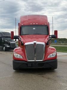 Kenworth T680 front view showing large chrome grille, red cab, black bumper, and dual side mirrors.