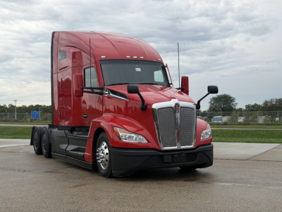 Red 2023 Kenworth T680 semi-truck in a showroom lot showing front grille, headlights, and cab with sleeper unit.