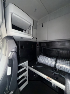 Kenworth T680 sleeper cab interior showing driver's seat, upper storage cabinet, bunk area with safety net and insulation, and side console panel.