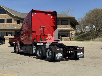 Kenworth T680 sleeper cab tractor in red, rear view showing dual rear axles and mud flaps with Konell logo, parked in lot with building in background.