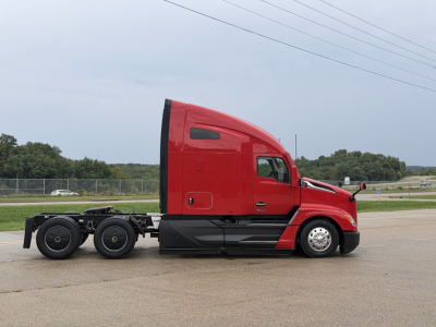 Kenworth T680 tractor unit side view showing red sleeper cab and chassis with quad rear axles on a parking lot.