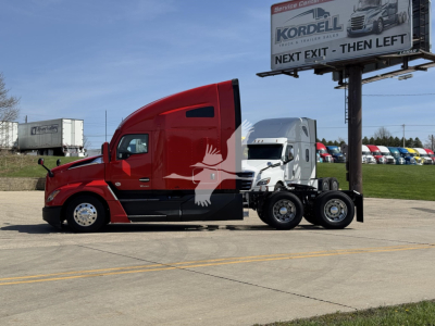 Kenworth T680 side view showing red aerodynamic cab and black chassis with six wheels; dealership sign in background with text