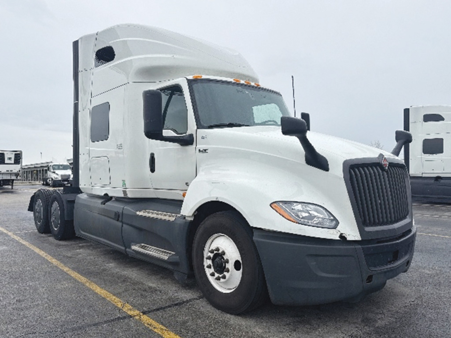 Truck cab area of a white 2023 International LT625 conventional sleeper, side view with front grille, headlights, and chrome mirrors visible.