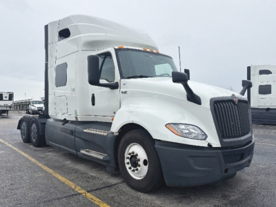 Truck cab area of a white 2023 International LT625 conventional sleeper, side view with front grille, headlights, and chrome mirrors visible.