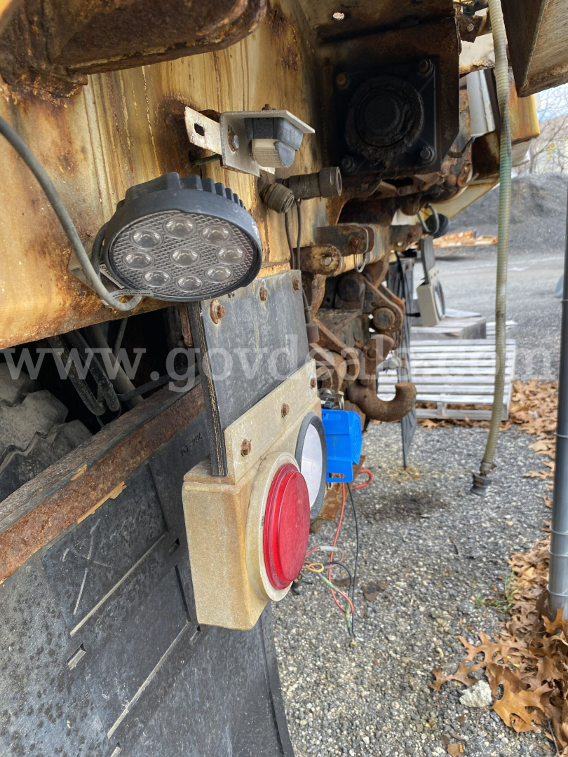 Dump truck rear with warning light, red circle indicator, and electrical connectors; visible text includes no explicit legible labels beyond generic truck components.