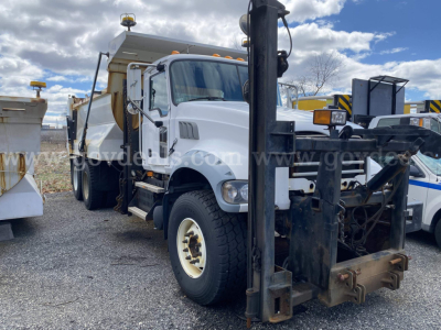 Dump truck front view showing Mack GU713 with attached front mount forks and hydraulic system. Visible text includes stock number and VIN partially on image watermark, and vehicle layout.
