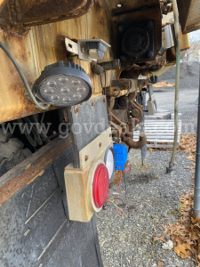 Dump truck rear with warning light, red circle indicator, and electrical connectors; visible text includes no explicit legible labels beyond generic truck components.