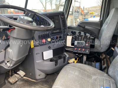 Mack GU713 truck interior shows steering wheel, instrument cluster, multiple switches, and control panel with levers. Visible text includes generic dashboard elements, no clear model or branding text legible.