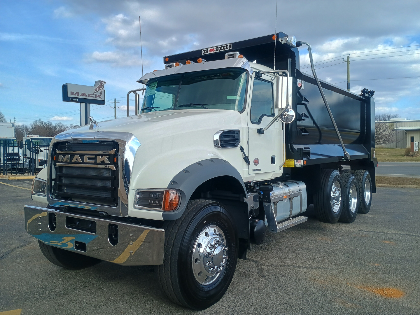 Mack GR84F dump truck in white cab with black dump bed, front chrome bumper, dual rear axles, and large side mirrors visible.