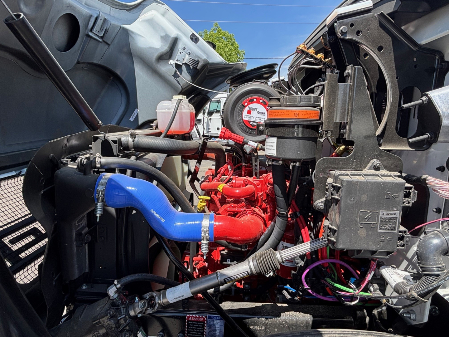 Mack MD6 engine bay showing red engine, blue coolant hose, various hoses, wiring harness, and diagnostic gauge cluster.