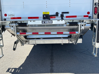 Rear view of a new Mack MD6 box truck showing a metal tailgate with Walters brand parts, reflective red/white stripes, and bumper hardware. Visible labels include Whiting and Walco.