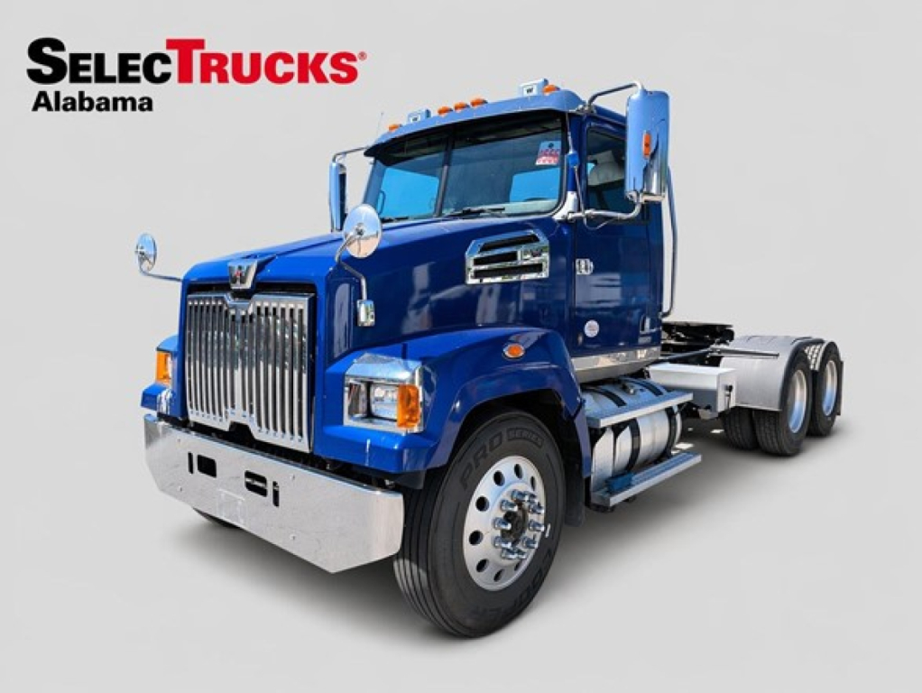 Western Star 4700 day cab truck in blue, front-left view showing chrome grille, bumper, dual exhaust stacks, and wheel hubs.