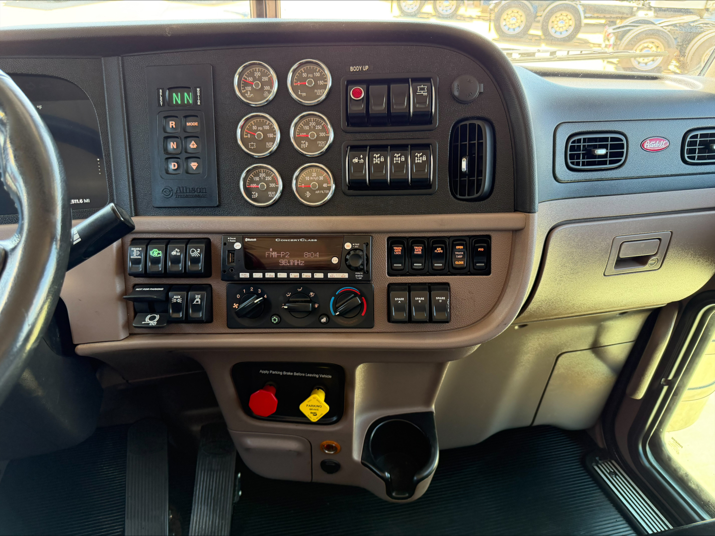 Truck cab dash panel with multiple gauges and controls in Peterbilt 389 interior, including circular gauges, climate controls, and toggle switches.