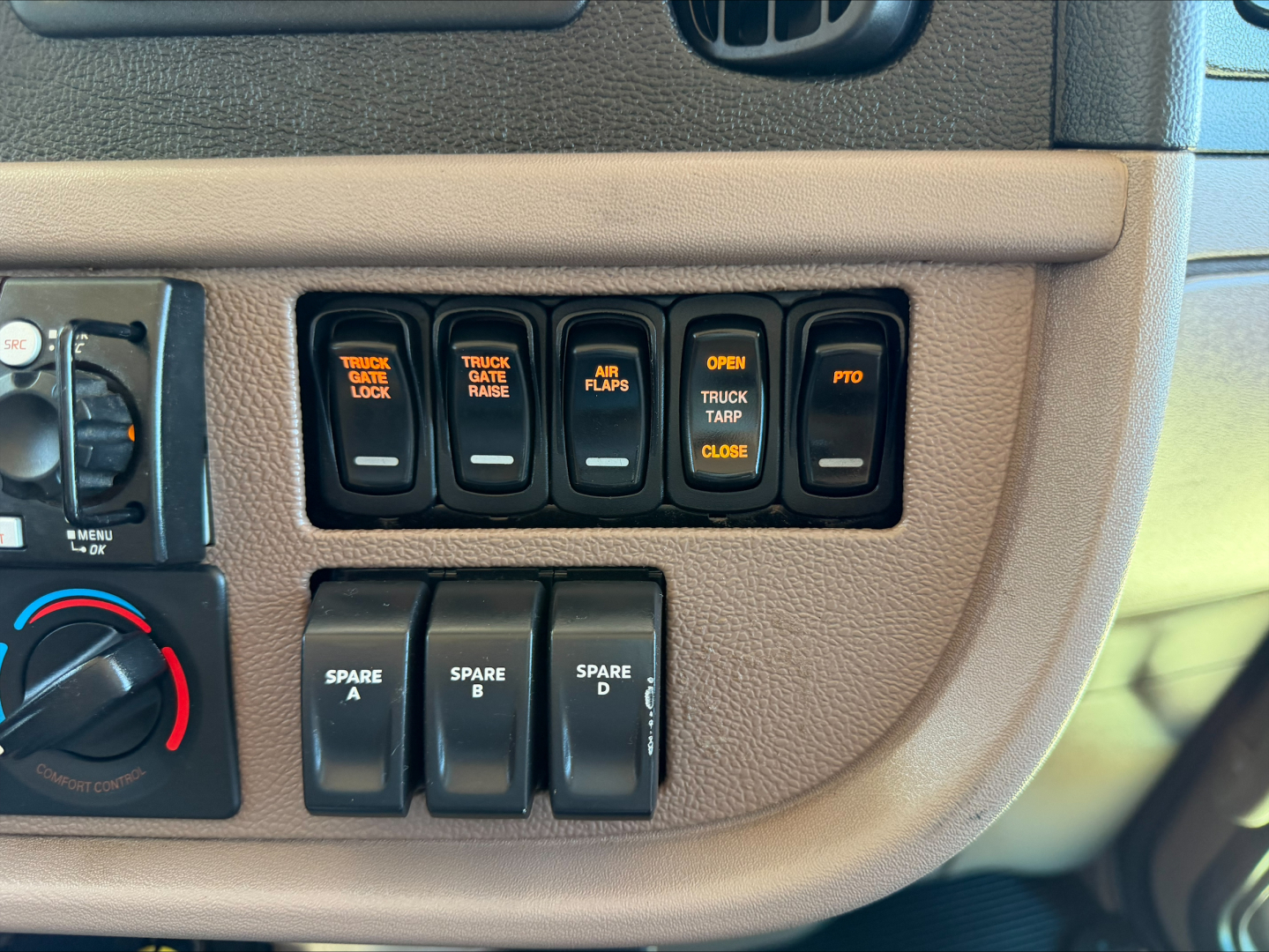 Truck dash panel with multiple switches labeled TRUCK LOCK, TRUCK GATE, AIR FLAPS, OPEN TRUCK TARP, CLOSE etc., plus spare A-D switches visible.