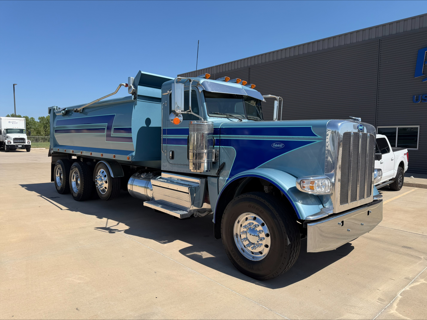 Peterbilt 389 dump truck in service shown from side-front angle with blue paint and chrome accents, dump bed visible.