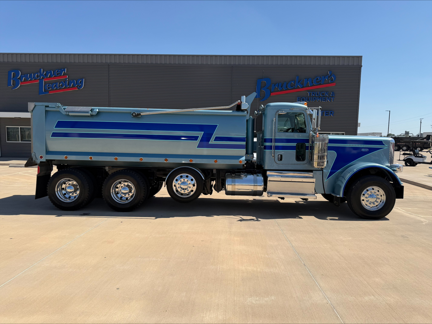 Truck showing Peterbilt 389 dump truck side view with blue and white paint and multiple rear axles.