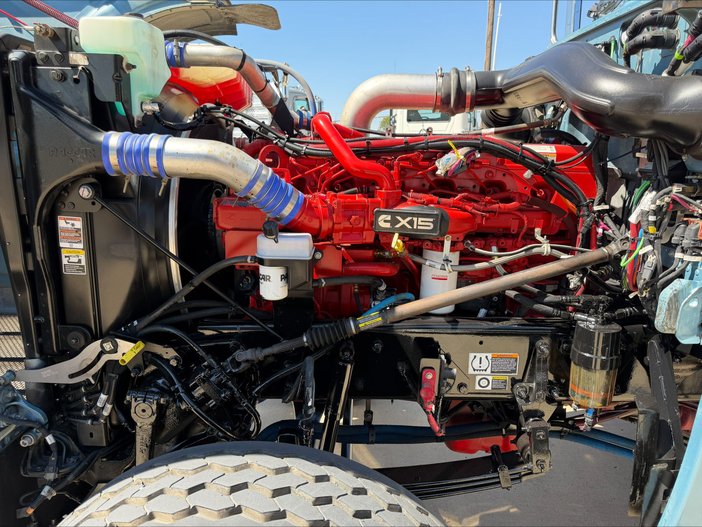 Peterbilt 389 engine bay with red CX15 diesel engine, surrounding hoses and components visible.