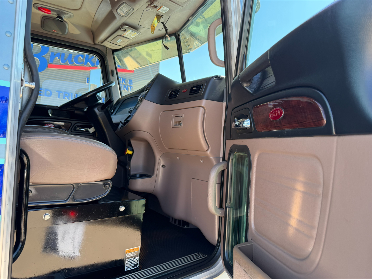 Peterbilt 389 truck interior cab view with steering wheel and dashboard; tan and black accents visible; entry door open.