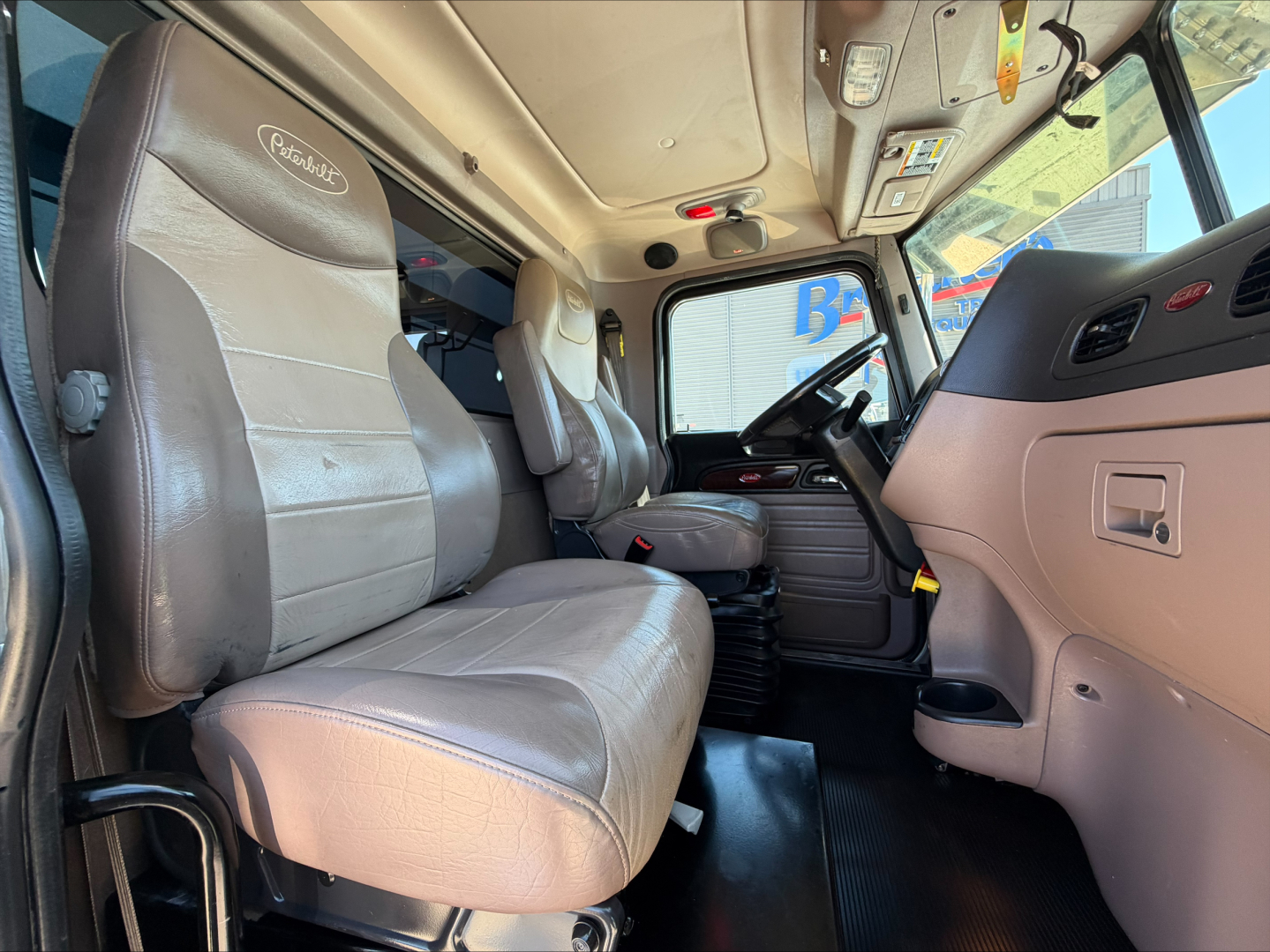 Peterbilt 389 truck cab interior showing driver and passenger seats with steering wheel and dashboard visible.