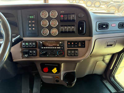 Truck cab dash panel with multiple gauges and controls in Peterbilt 389 interior, including circular gauges, climate controls, and toggle switches.