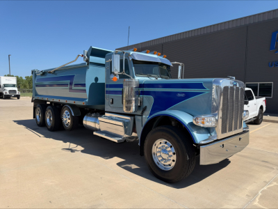 Peterbilt 389 dump truck in service shown from side-front angle with blue paint and chrome accents, dump bed visible.