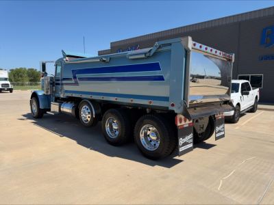 Peterbilt 389 dump truck with blue and silver dump body and chrome wheels, rear view showing tailgate and mud flaps.