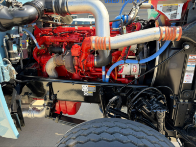 Peterbilt 389 engine bay with red engine, large silver intake piping, blue hoses, and black chassis