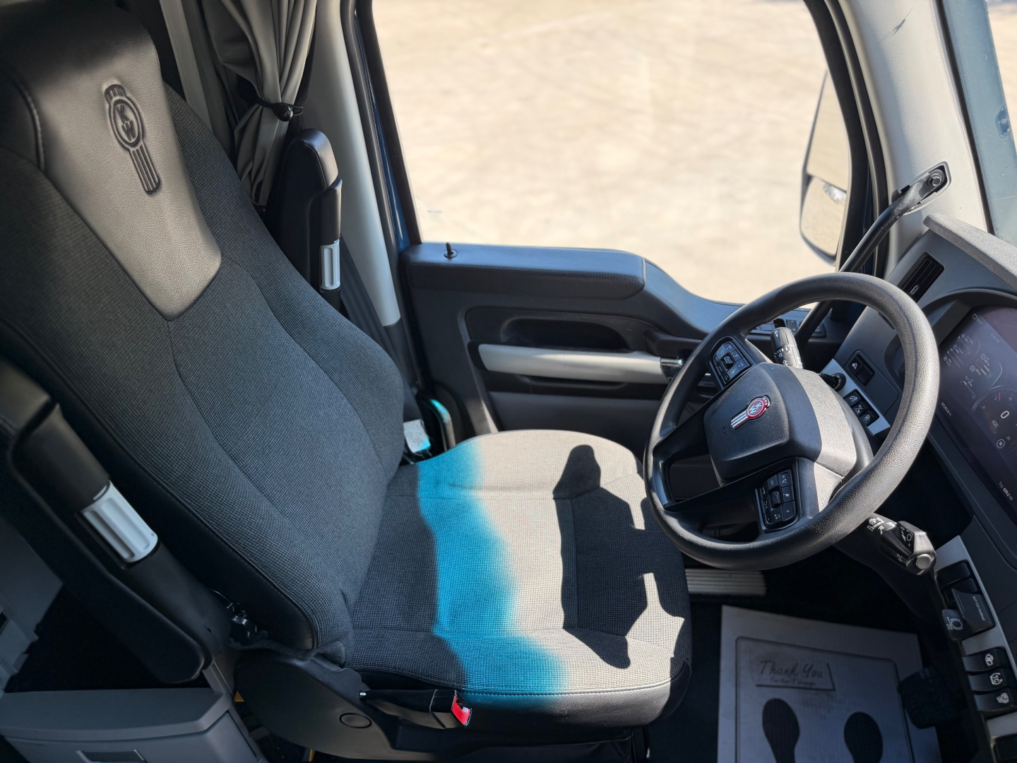 Truck interior of a 2023 Kenworth T680 seat and steering wheel visible in cab with dashboard controls.