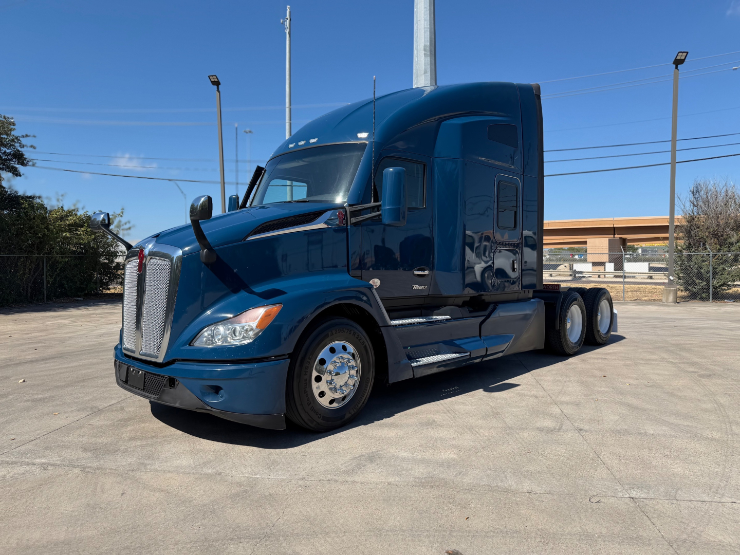 Kenworth T680 2023 conventional sleeper tractor in blue, side view showing front grille, headlights, aerodynamic mirrors, and dual rear axles.