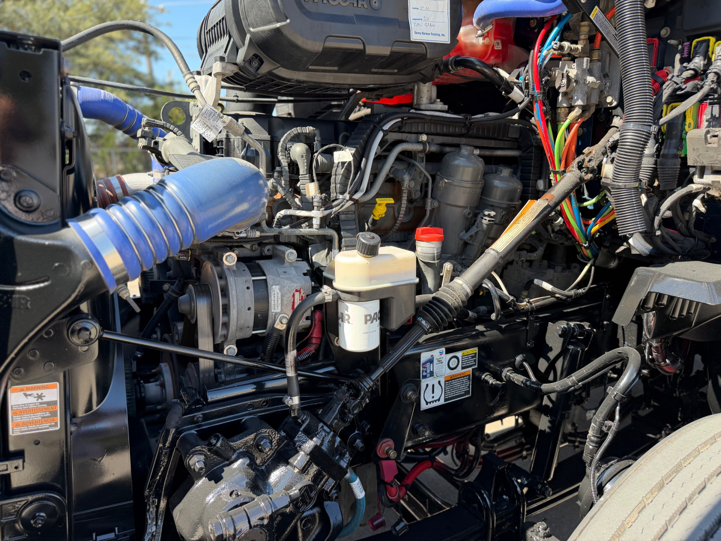 Kenworth T680 engine bay showing turbocharger, blue intake hose, multiple Electrical wires, fluid reservoirs, and engine components.