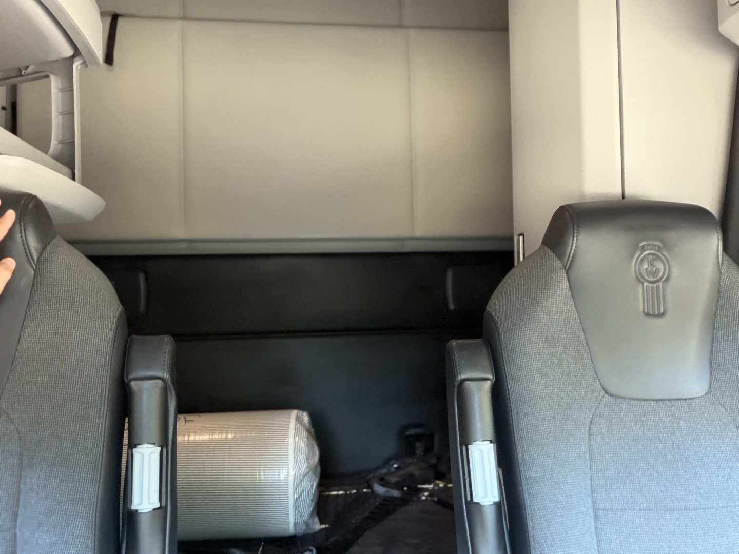 Truck interior cabin with two seats and sleeper area; visible are seat backs, overhead panel, and storage area behind seats; air filter or cylindrical object on floor between seats.