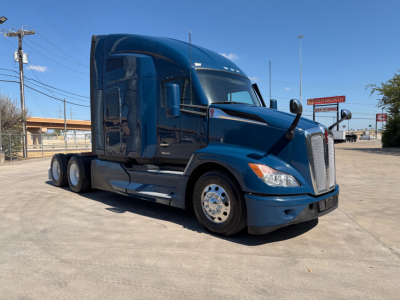 Kenworth T680 blue sleeper tractor truck in a dealership lot, side view showing cab, chrome wheels, and tandem rear axles.