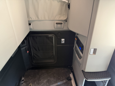 Cabin entry area of a 2023 Kenworth T680 showing a black lower storage compartment and step with textured tread, side panels, and a vertical control panel area.