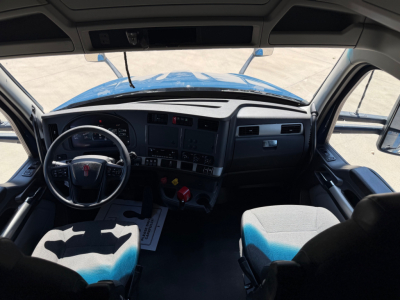 Cab interior of a blue Kenworth truck showing steering wheel, dashboard, and two front seats.