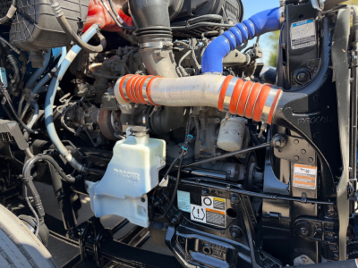 Kenworth T680 engine bay showing coolant reservoir, orange intake hose, blue hose, and black engine components.