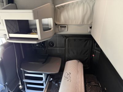 Cab interior of Kenworth T680 sleeper area showing elevated bunk, shelf, and desk setup with light gray panels and storage compartments.