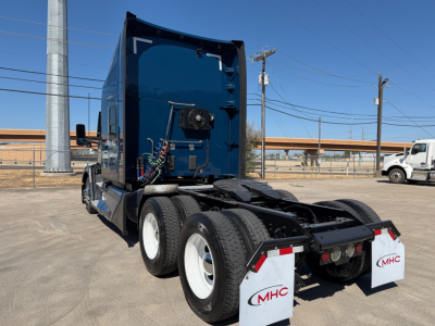 Kenworth T680 truck rear view showing fifth wheel and dual rear axles, blue cab, white mud flaps with MHC logo, and rear lighting.