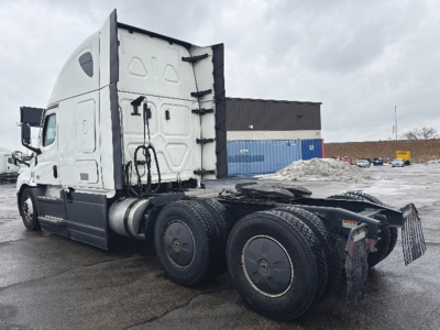 Truck chassis and cab of a 2023 Freightliner Cascadia 126 with sleeper cab, side view showing rear wheel axles and fifth wheel mount.
