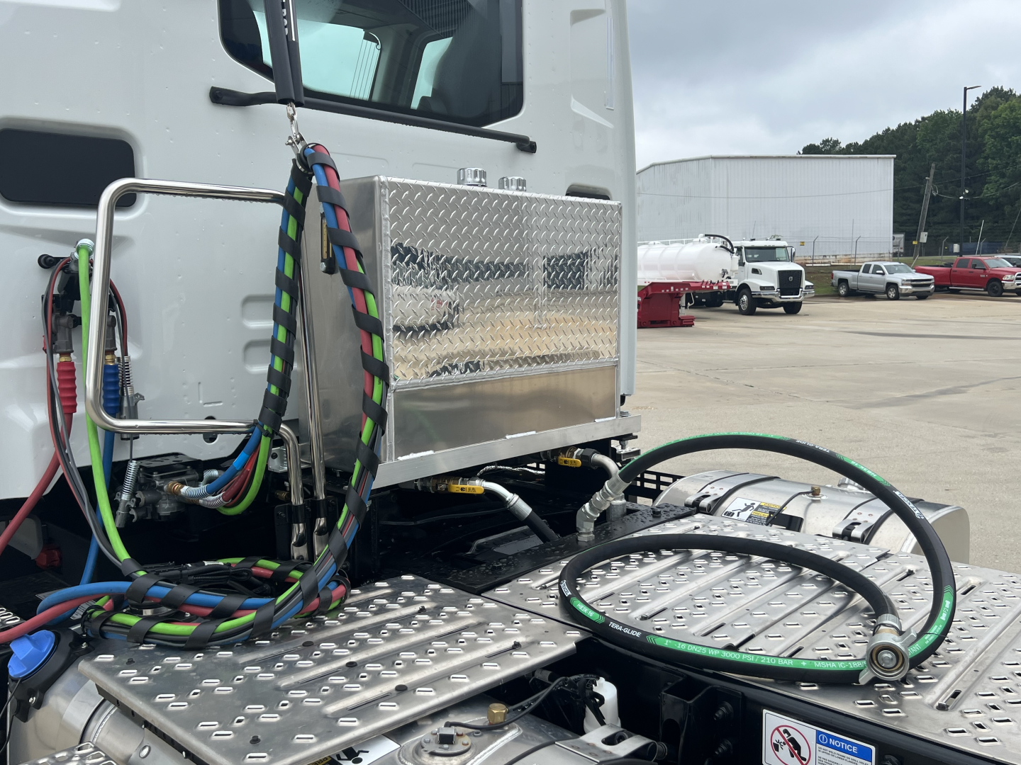 Mack AN64T truck cab area with diamond plate steps and colorful braided cables, fuel lines and hoses visible near the engine bay area.