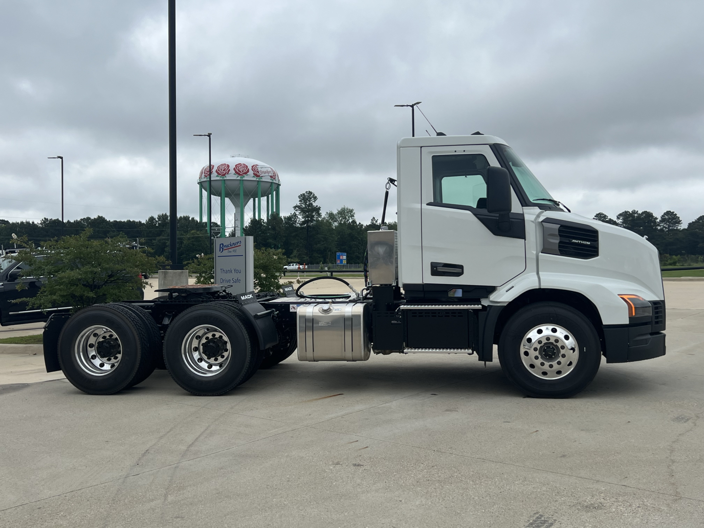 White Mack AN64T conventional daycab truck side view showing cab, fuel tanks, and dual rear axles with wheels. No visible text legible on truck.